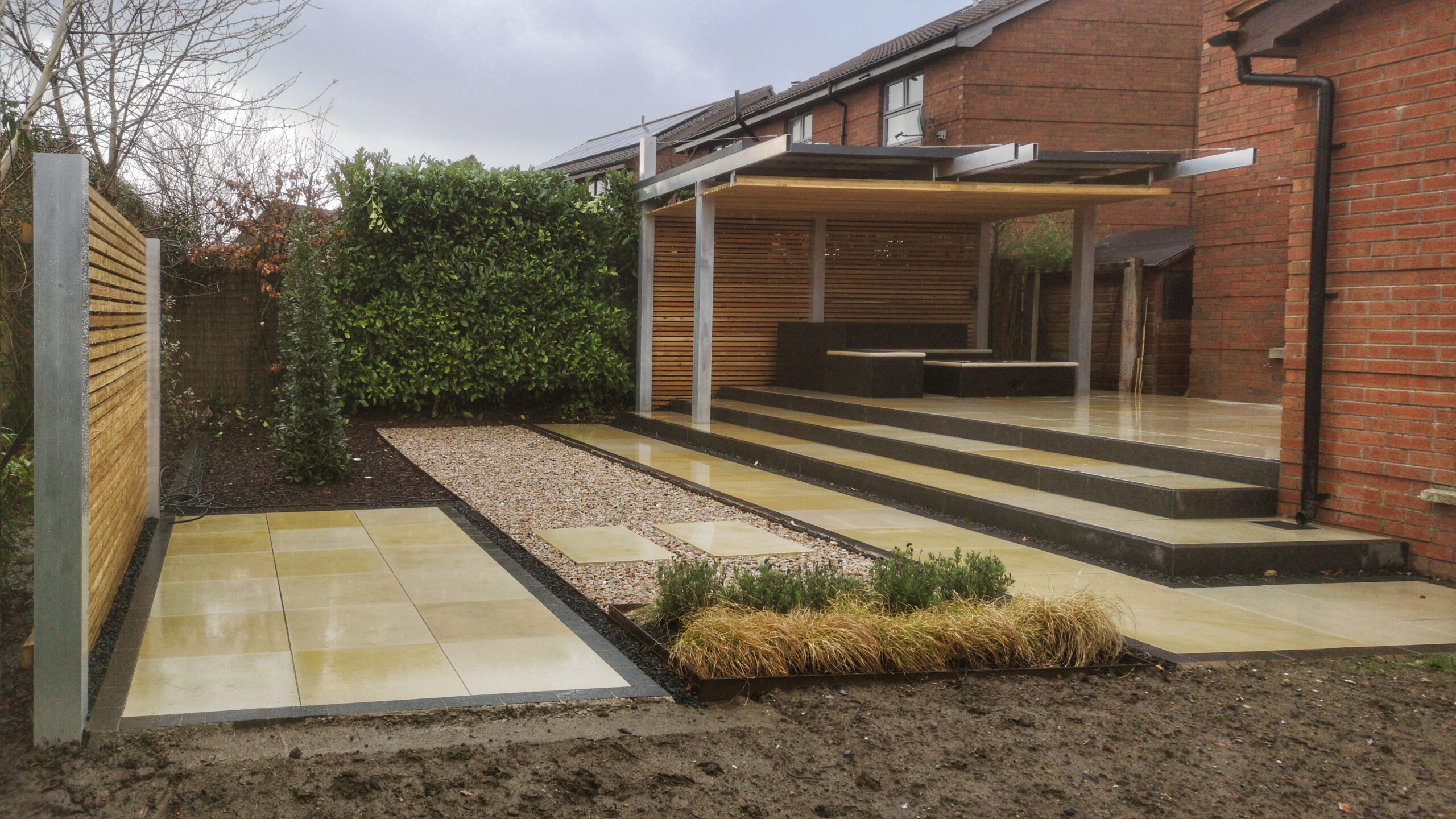 Sandstone patio with an aluminium pergola, gas fire pit and larch screening.