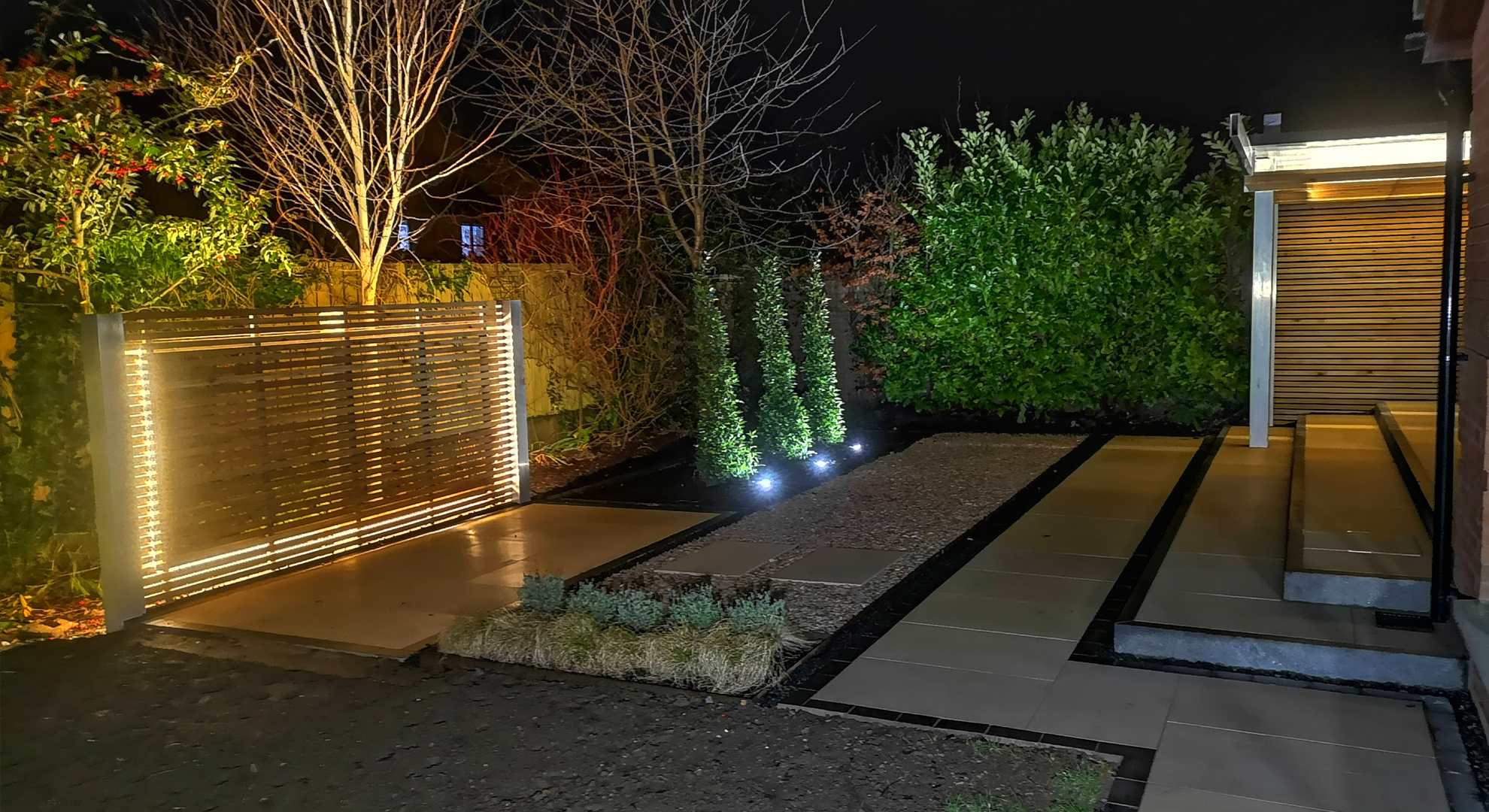 Bay totems lit up at night in contemporary sandstone and granite patio.